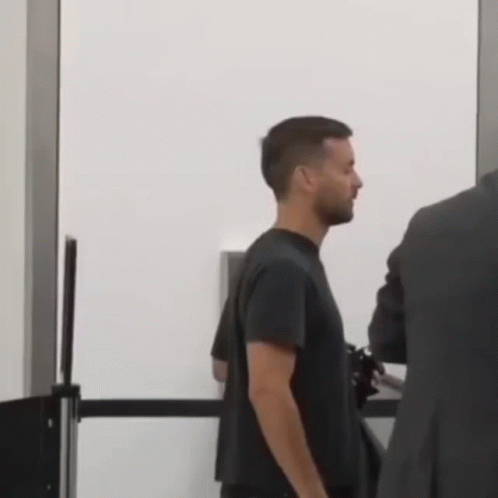 A Man In A Black Shirt Is Standing Next To A Man In A Suit At A Security Checkpoint . GIF