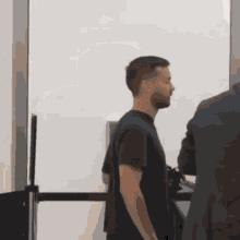 A Man In A Black Shirt Is Standing Next To A Man In A Suit GIF