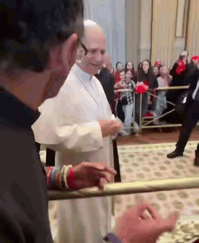 A Man In A Black Shirt Is Standing Next To A Man In A White Robe And Talking To Him . GIF
