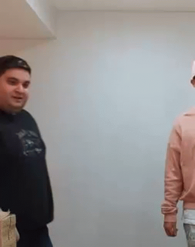 A Man In A Black Shirt Is Standing Next To A Woman In A Pink Sweater . GIF