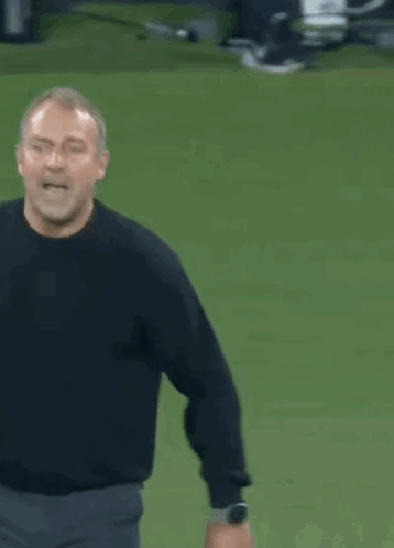 A Man In A Black Shirt Is Standing On A Field With His Arms Outstretched GIF