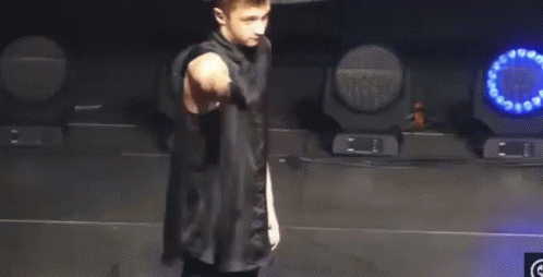 A Man In A Black Shirt Is Standing On A Stage With A Microphone In His Hand . GIF