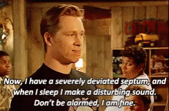 A Man In A Black Shirt Is Talking About A Disturbing Sound While Standing In A Room . GIF