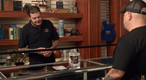 A Man In A Black Shirt Is Talking To Another Man In A Shop GIF