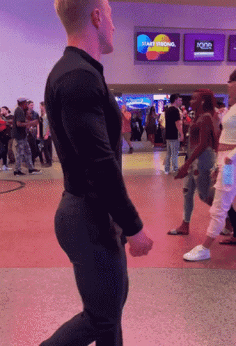 A Man In A Black Shirt Is Walking In Front Of A Sign That Says Start Thinking GIF