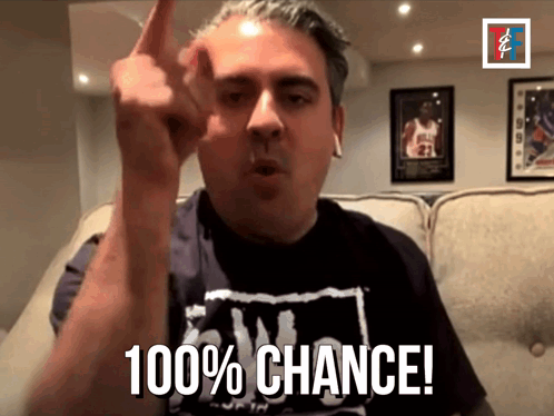 a man in a black shirt says 100 % chance in front of a couch
