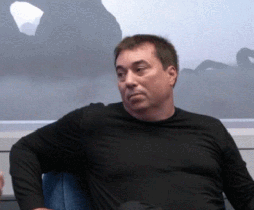 A Man In A Black Shirt Sits In A Chair GIF