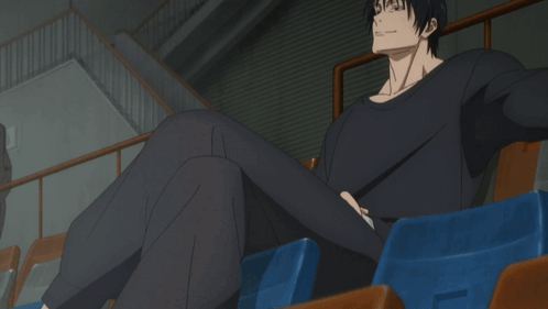 A Man In A Black Shirt Sits In A Stadium With His Legs Crossed GIF