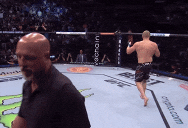A Man In A Black Shirt Stands In A Boxing Ring With The Word Ufc On The Ground GIF