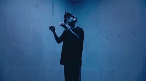 A Man In A Black Shirt Stands In A Dark Room GIF