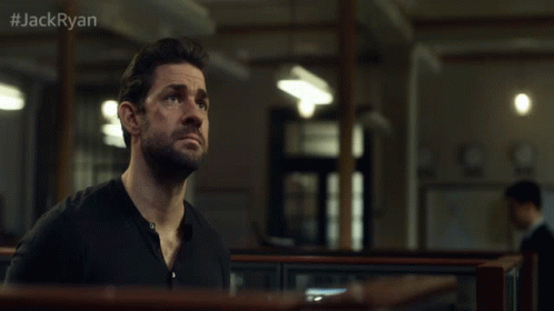 A Man In A Black Shirt Stands In A Dark Room With #Jackryan On The Bottom GIF