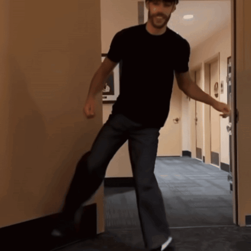 A Man In A Black Shirt Stands In A Hallway GIF