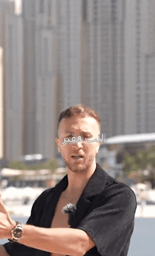 a man in a black shirt stands in front of a city skyline with arabic writing on it