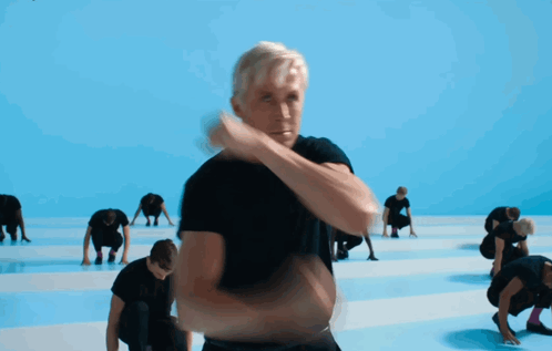 A Man In A Black Shirt Stands In Front Of A Group Of People GIF
