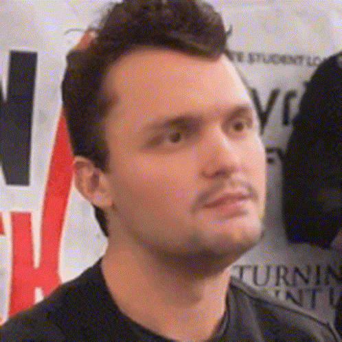 A Man In A Black Shirt Stands In Front Of A Sign That Says Turn GIF