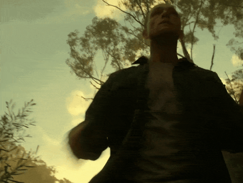 A Man In A Black Shirt Stands In Front Of A Tree GIF