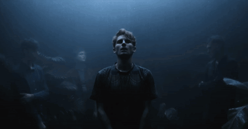 A Man In A Black Shirt Stands In The Dark GIF