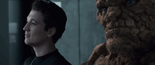 A Man In A Black Shirt Stands Next To A Statue Of A Face GIF