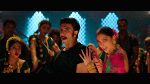 A Man In A Black Shirt Stands Next To A Woman In A Pink And Green Dress GIF