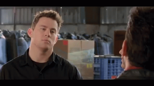 A Man In A Black Shirt Talks To Another Man In A Warehouse . GIF