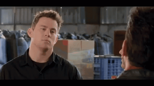 A Man In A Black Shirt Talks To Another Man In A Warehouse . GIF