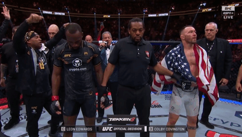 A Man In A Black Shirt That Says Ufc Stands Next To A Man In An American Flag GIF