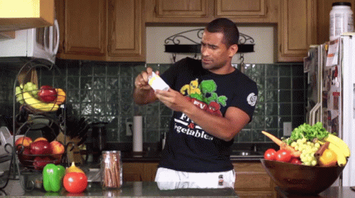 A Man In A Black Shirt That Says Vegetables Is Standing In The Kitchen GIF