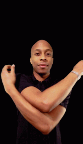A Man In A Black Shirt With His Arms Crossed Looks At The Camera GIF
