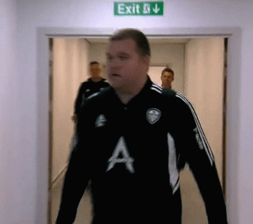 a man in a black shirt with the letter a on it walks through an exit sign