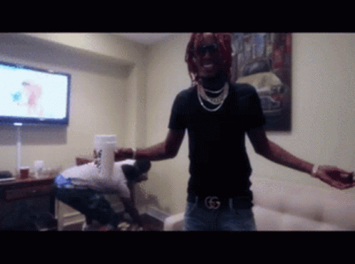 A Man In A Black Shirt With The Letter G On His Belt Stands In A Room GIF