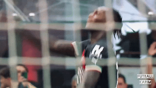 A Man In A Black Shirt With The Letter K On It Is Behind A Fence GIF