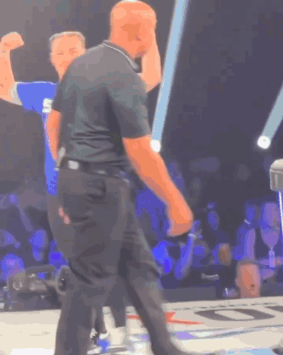 A Man In A Black Shirt With The Letter S On It Stands In Front Of A Crowd GIF