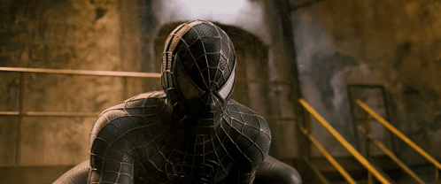 A Man In A Black Spiderman Costume Is Sitting On A Staircase GIF
