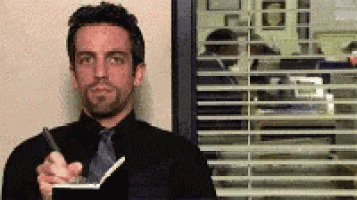 A Man In A Black Suit And Tie Is Holding A Pen And A Notebook GIF
