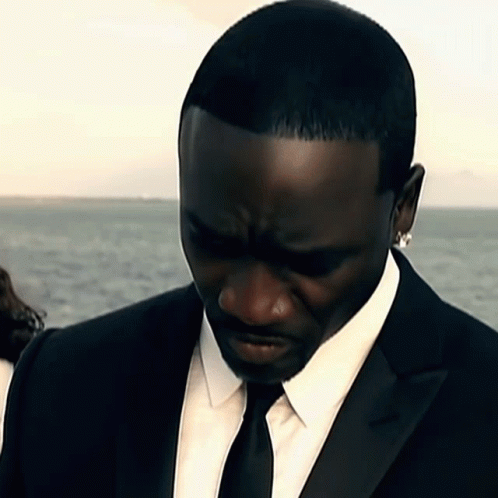 A Man In A Black Suit And Tie Looks Down GIF