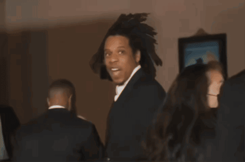 A Man In A Black Suit And White Tie Is Standing In A Room GIF