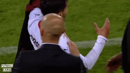 A Man In A Black Suit Holds A Soccer Player In A White Jersey That Says Karim GIF