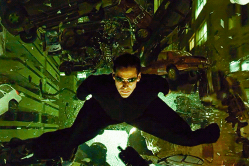 A Man In A Black Suit Is Flying Through The Air In A City GIF