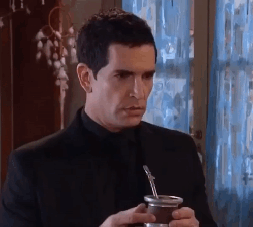 A Man In A Black Suit Is Holding A Cup Of Yerba Mate . GIF