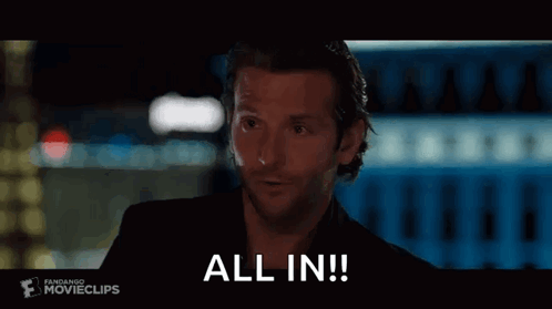 A Man In A Black Suit Is Holding A Glass Of Wine And Says `` All In '' . GIF