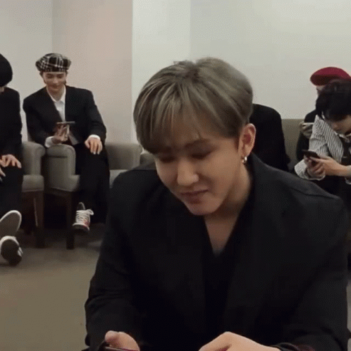 A Man In A Black Suit Is Sitting In A Room With Other Men GIF