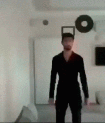 A Man In A Black Suit Is Standing In A Room With A Circle On The Wall . GIF