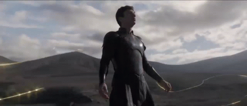 A Man In A Black Suit Is Standing In Front Of A Mountain Range In A Desert . GIF