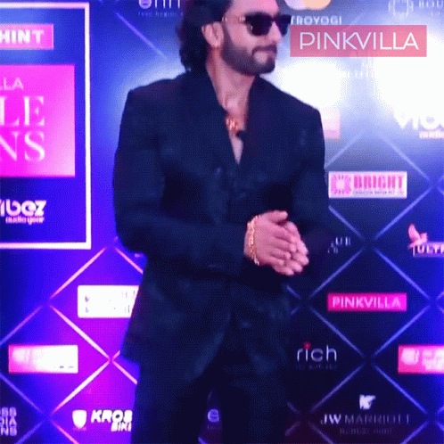 A Man In A Black Suit Is Standing In Front Of A Pinkvilla Sign GIF