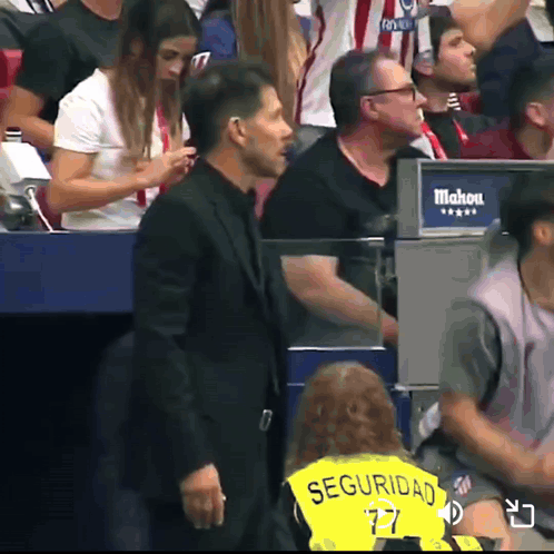 A Man In A Black Suit Is Standing In Front Of A Sign That Says Mahou GIF