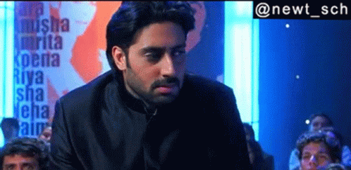 A Man In A Black Suit Is Standing In Front Of A Sign That Says Riya GIF