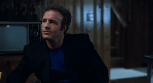 A Man In A Black Suit Is Talking To Another Man In A Blue Shirt GIF