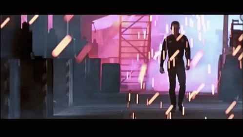 A Man In A Black Suit Is Walking Through A Room With A Lot Of Lights Coming Out Of It GIF