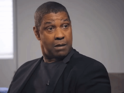 A Man In A Black Suit Looks At The Camera With A Serious Look On His Face GIF
