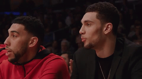 A Man In A Black Suit Sits Next To A Man In A Red Shirt GIF